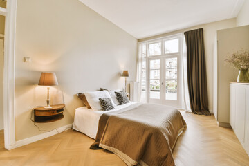 a bedroom with wood flooring and white walls, including a large bed in the room has a brown blanket on it