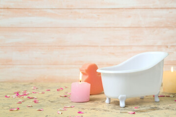 Small bathtub, burning candles, sponge and flower petals on table