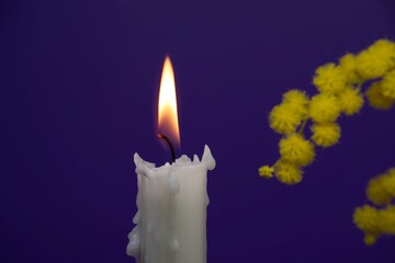 Candle flame and yellow mimosa flowers over blue