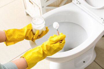 Woman in rubber gloves cleaning toilet bowl with baking soda