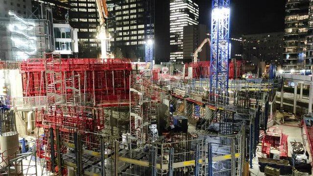 Night sight of skyscraper construction site with cranes and scaffolding, wide panning shot
