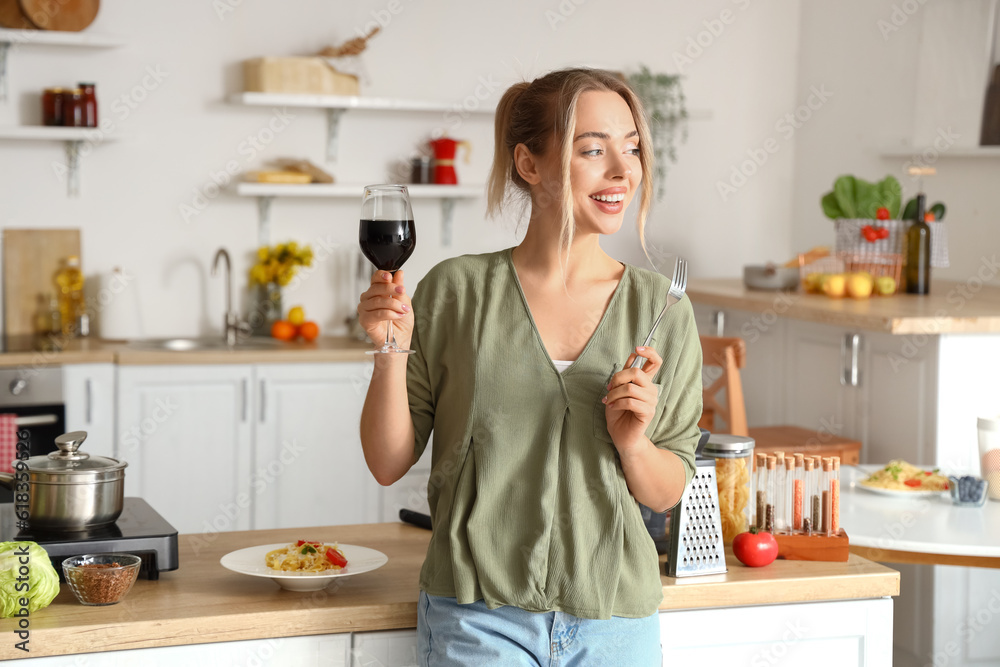 Canvas Prints young woman with glass of wine eating tasty pasta in kitchen