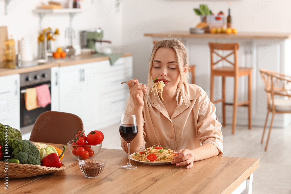 Wall mural young woman eating tasty pasta in kitchen