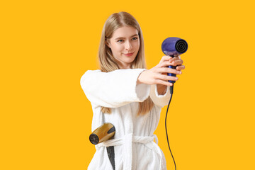 Young blonde woman with hair dryers on yellow background