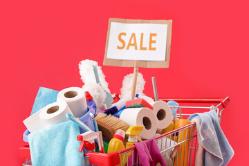 Shopping cart full of cleaning supplies and word SALE on red background