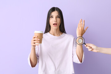 Young woman in wristwatch holding cup of coffee and female hand with magnifiers on lilac background