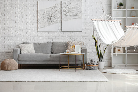 Interior of light living room with hammock, grey sofa and coffee table