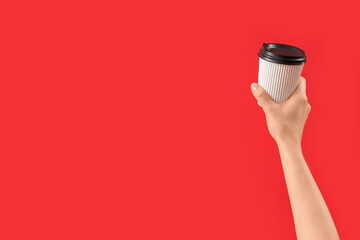 Female hand with takeaway cup of coffee on red background
