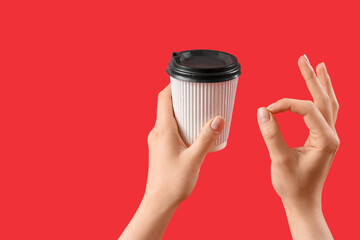 Woman holding takeaway cup of coffee and showing OK gesture on red background