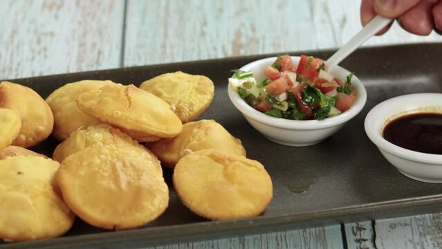 Sopaipillas hand placing pebre, zapallo or zapallito in rectangular plate on wooden table, bowl chancaca. Horizontal video Concept of typical Chilean food
