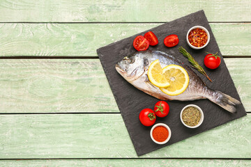 Slate board of raw dorado fish with lemon, tomatoes and spices on green wooden background