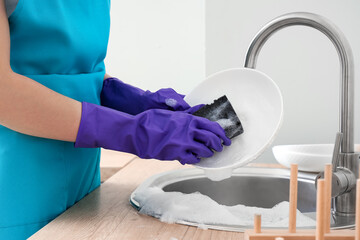 Woman in purple rubber gloves washing dishes with sponge