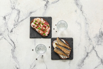 Shots with cold vodka and tasty sandwiches on white marble background