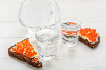 Shots of cold vodka and bread with red caviar on white wooden background