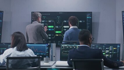 Multiethnic IT technical specialists monitor database server and real-time analysis charts on computers in monitoring office. Software engineers work with blockchain network on big digital screens. - Powered by Adobe