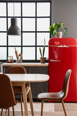 Interior of modern kitchen with dining table, red fridge and window