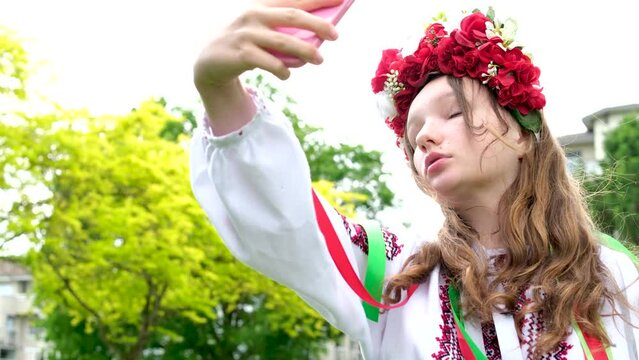 Ukrainian woman in a traditional folk image looks at the phone taking a selfie. Looks in the mirror beauty beautiful wreath with many white flowers beauty of a teenager girl Ukraine No war joy nature