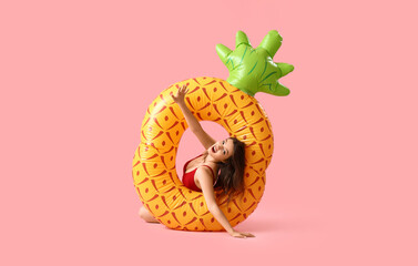 Young woman with swim ring in shape of pineapple on pink background
