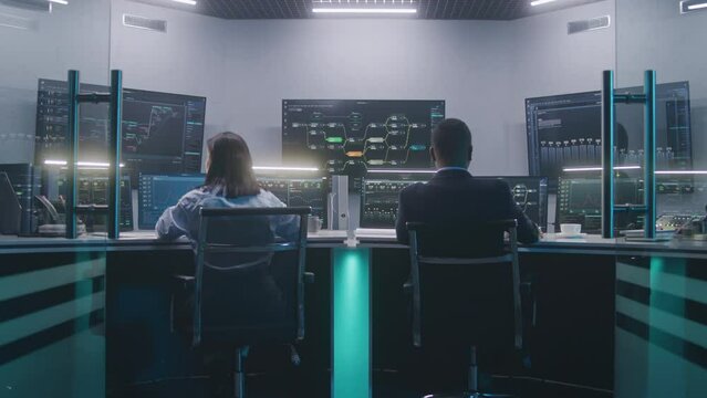 Software programmers work on computers. IT technical specialist enters modern monitoring control room, works with data server, real-time analysis charts and blockchain network on big digital screens.