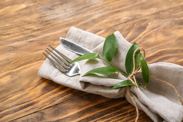 Napkin with cutlery and plant branch on wooden table, closeup