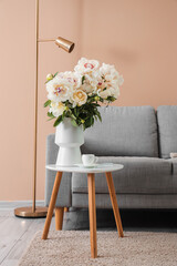 Vase of white peonies with coffee table, couch and floor lamp near beige wall
