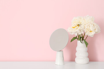 Vase of white peonies and mirror on dresser near pink wall