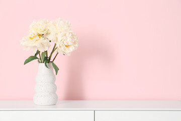 Vase of white peonies on dresser near pink wall