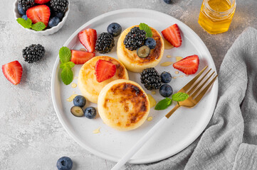 Cottage cheese pancakes, syrniki, ricotta fritters with fresh berries, honey and sour cream on a gray concrete background. Healthy and delicious breakfast. Top view, copy space.