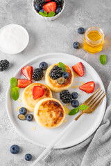 Cottage cheese pancakes, syrniki, ricotta fritters with fresh berries, honey and sour cream on a gray concrete background. Healthy and delicious breakfast. Top view, copy space.
