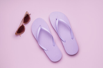 Lilac flip-flops with sunglasses on color background