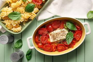 Baking dish with tasty tomatoes, feta cheese and pasta on green wooden background