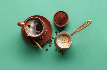 Cezve and cup decorated with coffee beans on green background