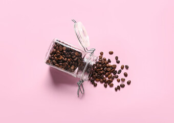 Glass jar with scattered coffee beans on pink background