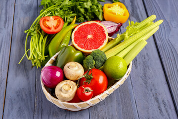 Basket with fresh ripe vegetables on blue wooden background, closeup
