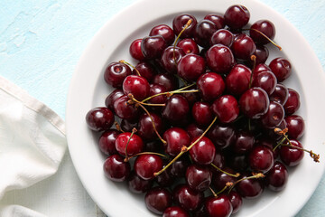 Plate with sweet cherries on blue background