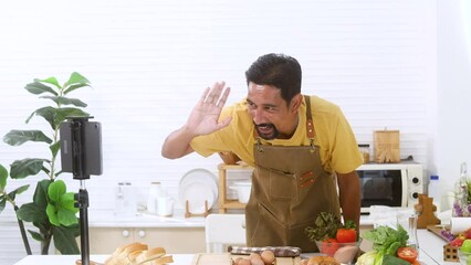 Attractive man with mustache blogger streaming live by notepad waving hand greeting to audiences tutorial cooking class with healthy food, modern lifestyle Asian male vlogger broadcast concept
