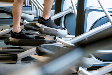 Male legs with sport footwear doing exercise on an elliptical trainer or air walker machine. Indoor cardio training workout and burn calories in fitness gym