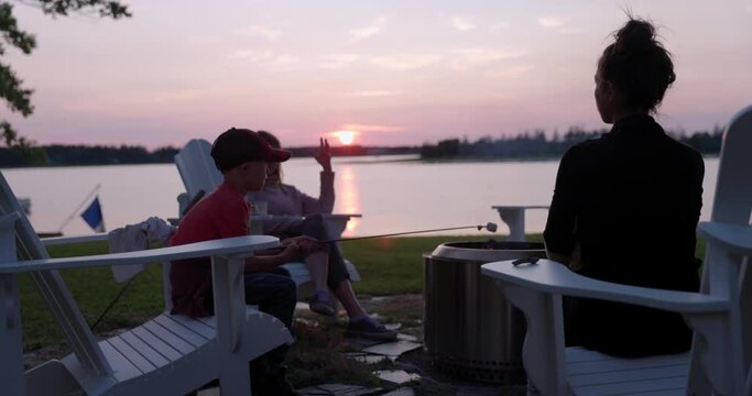Family sitting outside in backyard cooking marshmallows on firepit at sunset - cottage vibes