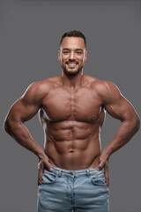 Fototapeta na wymiar Charming and muscular male model with a dazzling smile poses shirtless against a neutral grey backdrop, emanating confidence and sex appeal