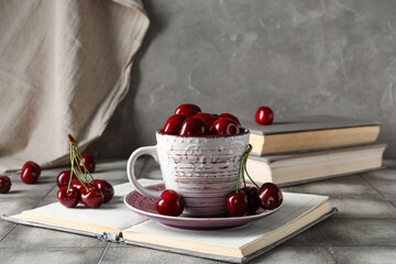 Cup with sweet cherries and books on grey tile table
