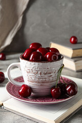 Cup with sweet cherries and books on grey background, closeup