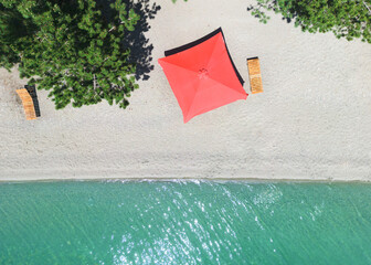 Aerial top view on the beach. Umbrellas, sunbeds, sand and ocean. Aerial view amazing empty white beach with red beach umbrella and turquoise clear water. Above