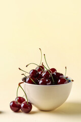 Bowl with sweet cherries on yellow background