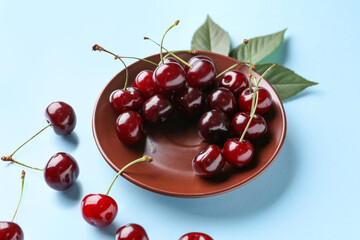 Plate with sweet cherries and leaves on blue background