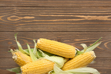 Wicker bowl with fresh corn cobs on wooden background
