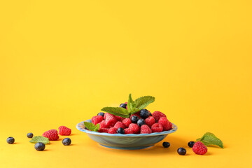 Plate with fresh raspberries and blueberries on yellow background