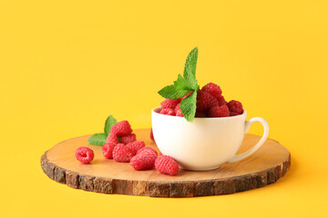 Cup and board with fresh raspberries on yellow background