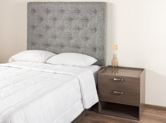 A bedroom featuring a bed with white bedspread and a grey fabric headboard, a nightstand situated beside it