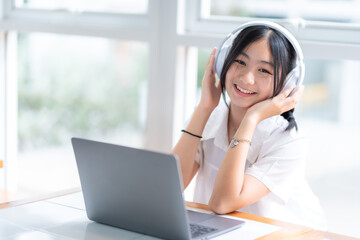 Happy of cute smiles Asian of attractive young Cute girl little wearing headphones and listening music using laptop computer working from at the cafe.Online education, elearning concept.