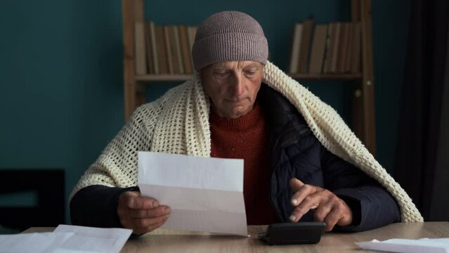 Upset poor bankrupt old man with no money freezing indoors at home, counting heating bill, reading power cut notification letter
